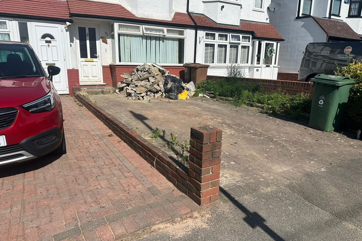 The same front garden before work: a bare driveway with no boundary fence and rubble piled by the house