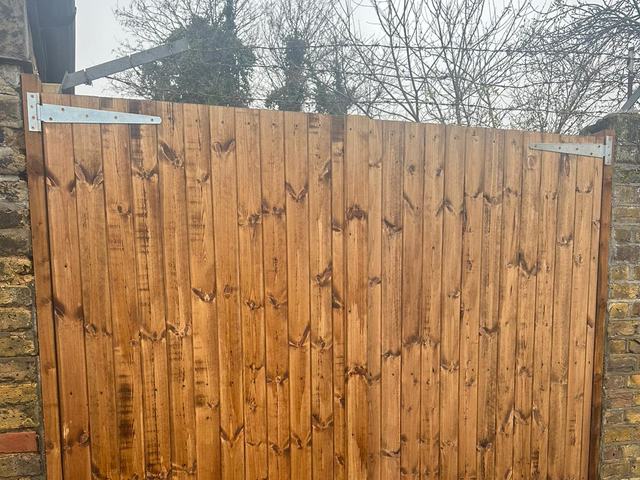 A pair of braced closeboard driveway gates hung on galvanised strap hinges between brick piers