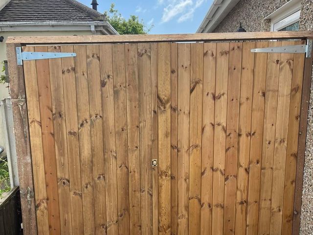 A pair of tall closeboard gates hung on galvanised hinges across a driveway
